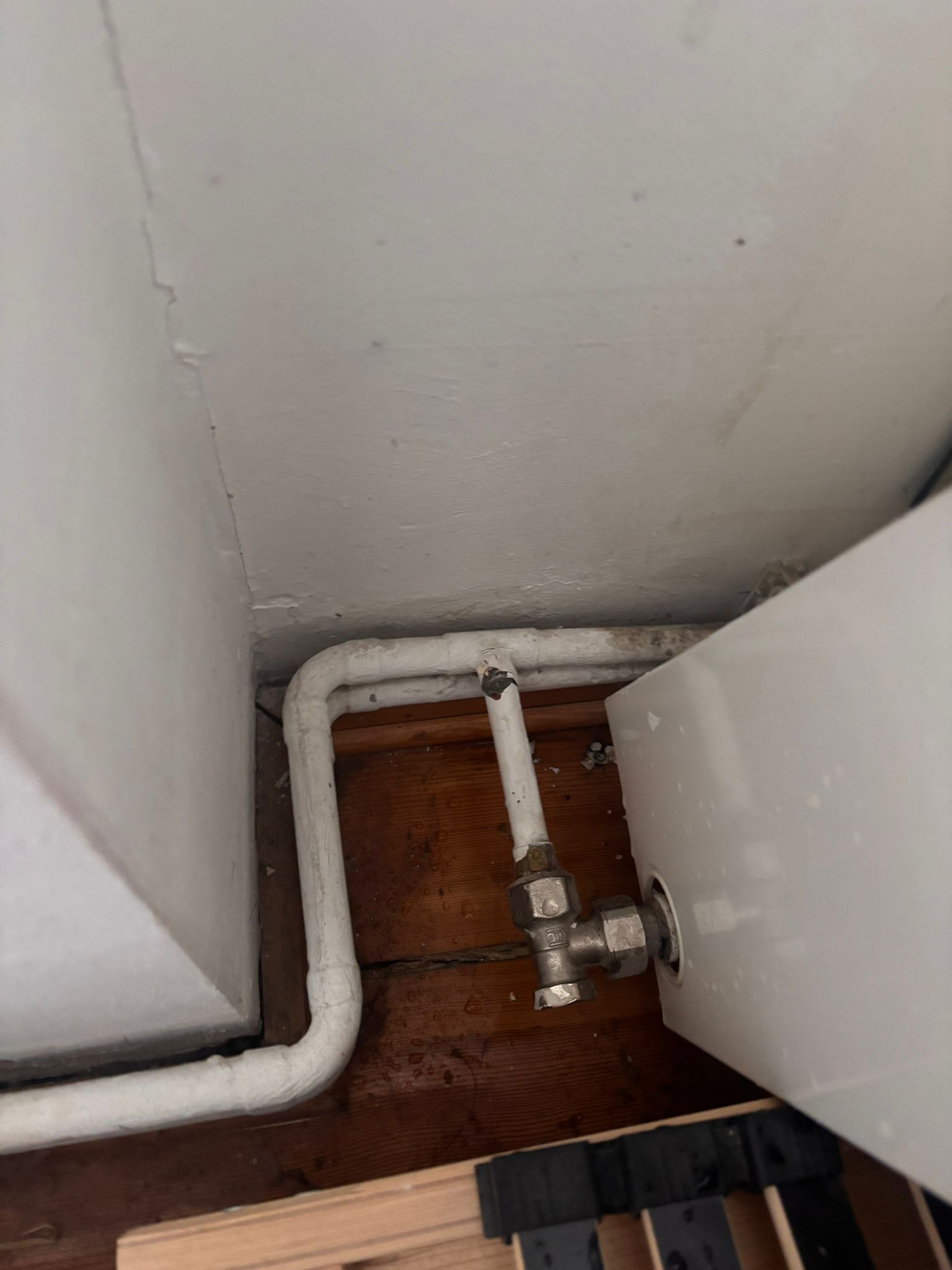 Weiß lackierte Heizungs- und Wasserleitungen mit Ventil an der Wand über einem Holzboden