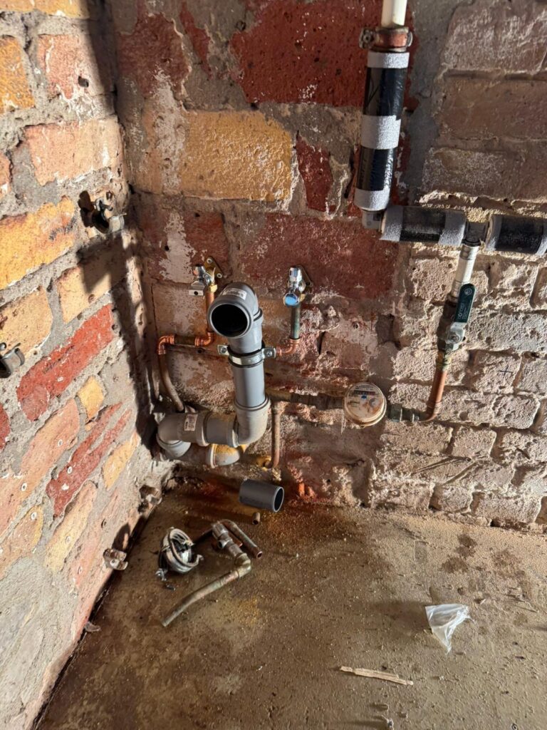 Freigelegte Wasser- und Abflussanschlüsse an einer Kellerwand aus Ziegelstein