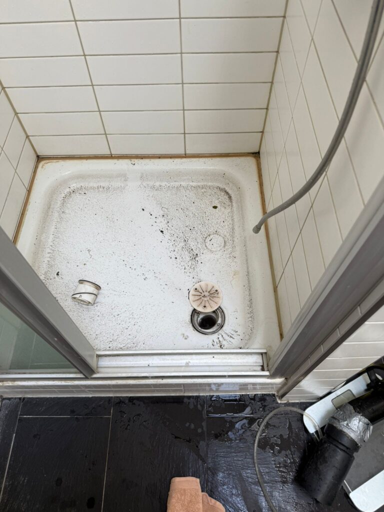 Verschmutzte Duschwanne mit geöffnetem Ablauf und ausgebautem Siphon daneben