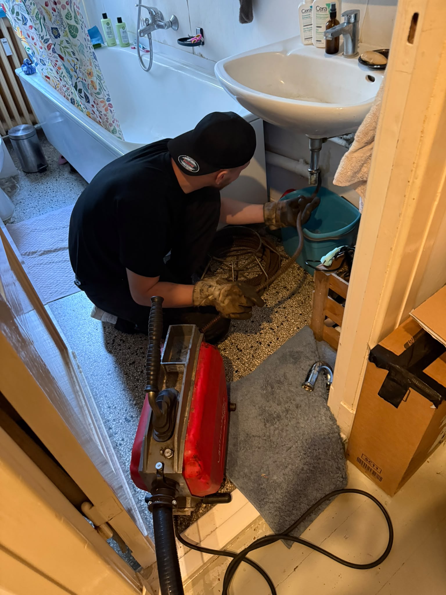 Monteur reinigt mit einer Rohrreinigungsmaschine den Abfluss unter einem Waschbecken im Altbau-Badezimmer