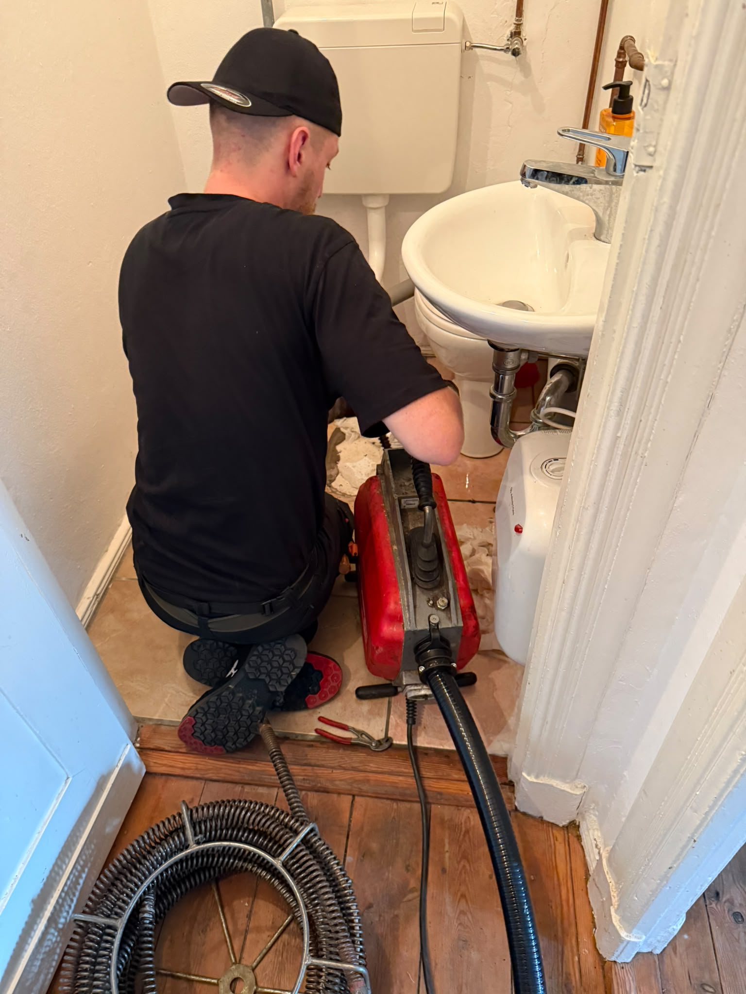 Monteur reinigt in einem kleinen Gäste-WC den Abfluss des Handwaschbeckens mit einer Rohrreinigungsmaschine