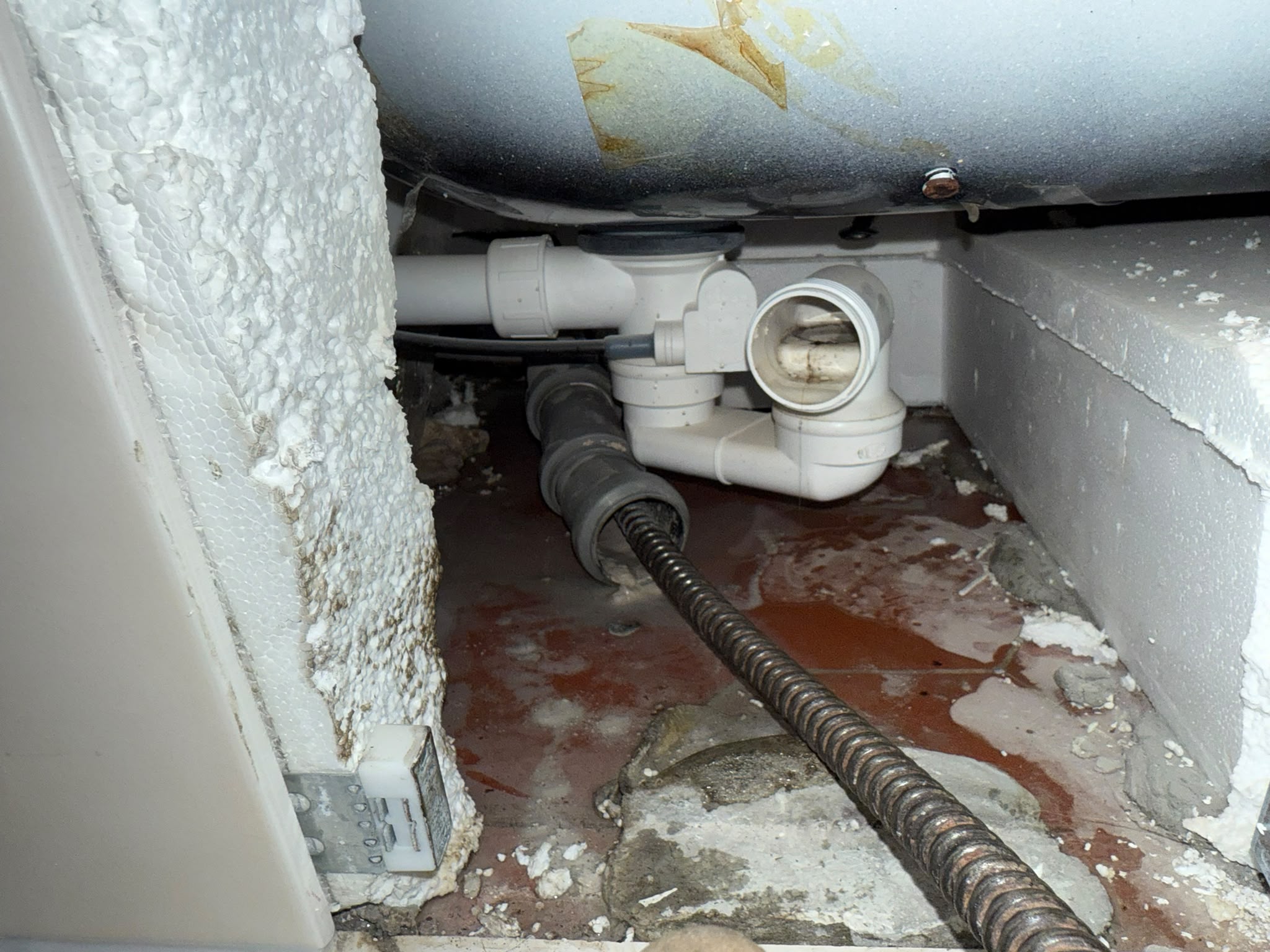 Abflussleitung unter einer Badewanne mit eingeführter Rohrreinigungsspirale, darunter Schmutzwasser