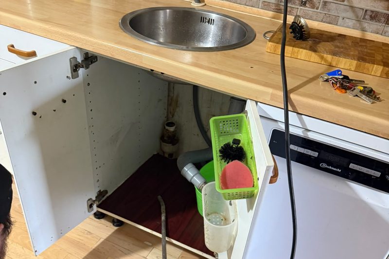 Klempner bei der Rohrreinigung unter einer Küchenspüle: Die Spirale einer Rohrreinigungsmaschine wird zum Abflussanschluss im Spülenschrank geführt