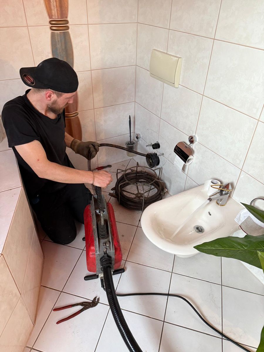 Monteur reinigt den Abflussanschluss eines abgebauten Wand-WCs mit einer elektrischen Rohrreinigungsmaschine
